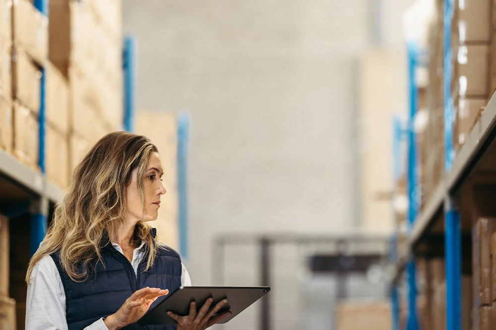 Gestionnaire vérifiant les stocks dans un entrepôt avec une tablette, optimisant la gestion de matériel et des inventaires.