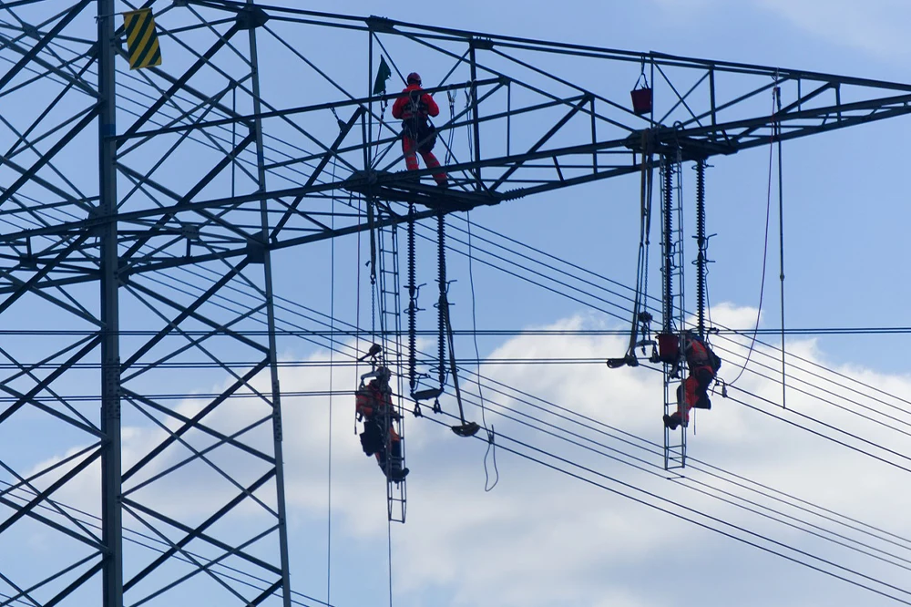 Techniciens en hauteur sur des lignes électriques, illustrant la gestion de matériel dans le secteur énergétique.