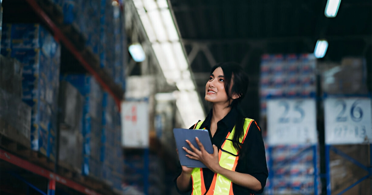 Femme dans un entrepôt utilisant TOOLTRACK pour la gestion du matériel, avec un appareil mobile
